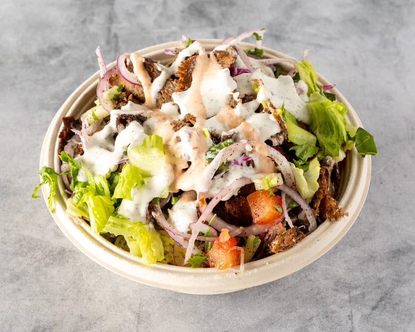 Gyro salad with meat, lettuce, tomatoes, red onions, and two sauces in a bowl.