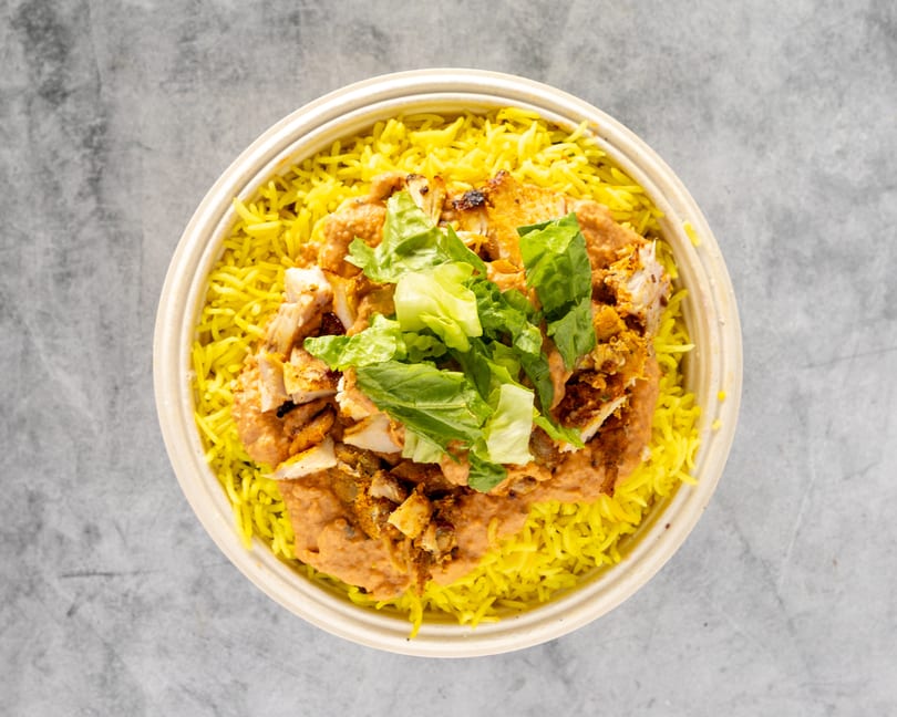 Overhead view of a chicken and rice bowl with yellow rice, chicken, sauce, and lettuce.