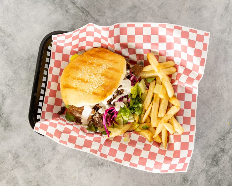 Doner kebab burger with white sauce, lettuce, red cabbage, and a side of fries in a basket.