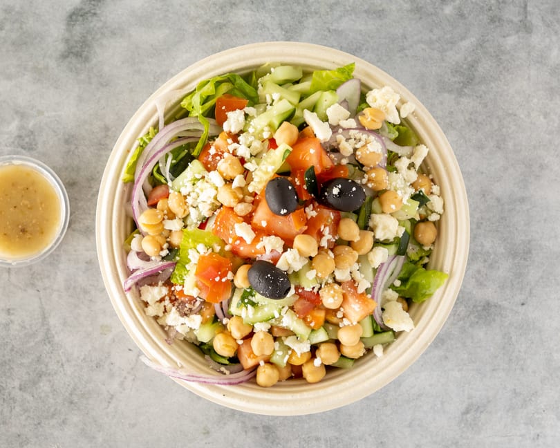 Overhead view of a colorful salad with chickpeas, olives, feta, and dressing on the side.